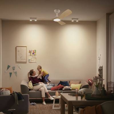 Une femme est assise avec un enfant sur un canapé dans un salon confortablement éclairé, décoré de tableaux muraux et de coussins colorés.