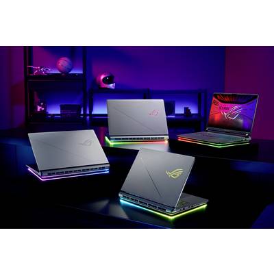 Quatre ordinateurs portables ASUS ROG avec des lumières RGB scintillantes sont disposés sur une table dans une pièce faiblement éclairée avec un éclairage d'ambiance bleu et violet.