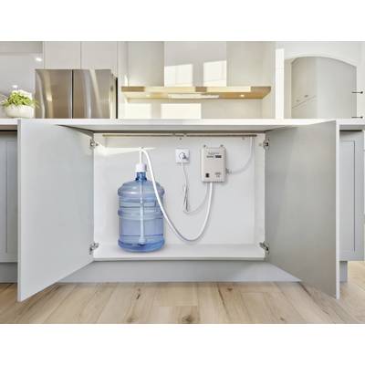 Vue sous l'évier d'un système de filtration d'eau installé, avec une grande bouteille d'eau bleue, des tuyaux de raccordement et une unité de contrôle.