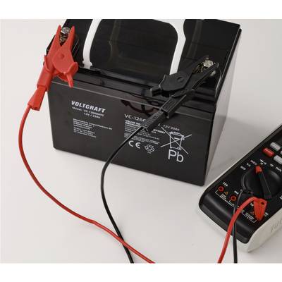 Une batterie de voiture avec des câbles de démarrage rouge et noir connectés, et un multimètre numérique mesurant la tension.