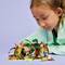 Un enfant aux cheveux châtain clair joue avec une cabane dans les arbres LEGO colorée et des figurines sur une table, exprimant concentration et curiosité.