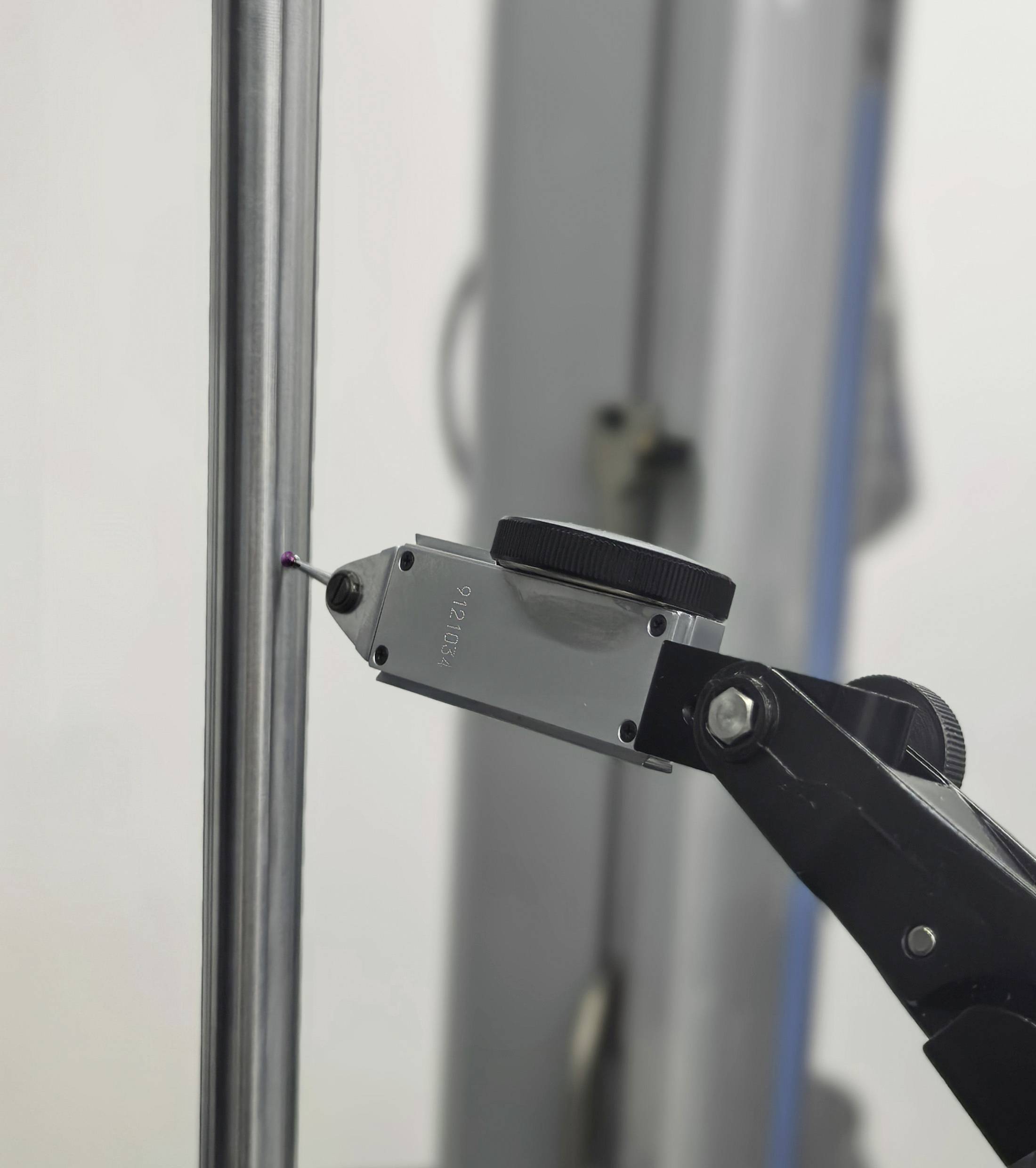 Un outil de mesure de précision doté d'un afficheur numérique entre en contact avec une tige métallique, probablement dans le cadre d'un processus de test ou d'étalonnage.