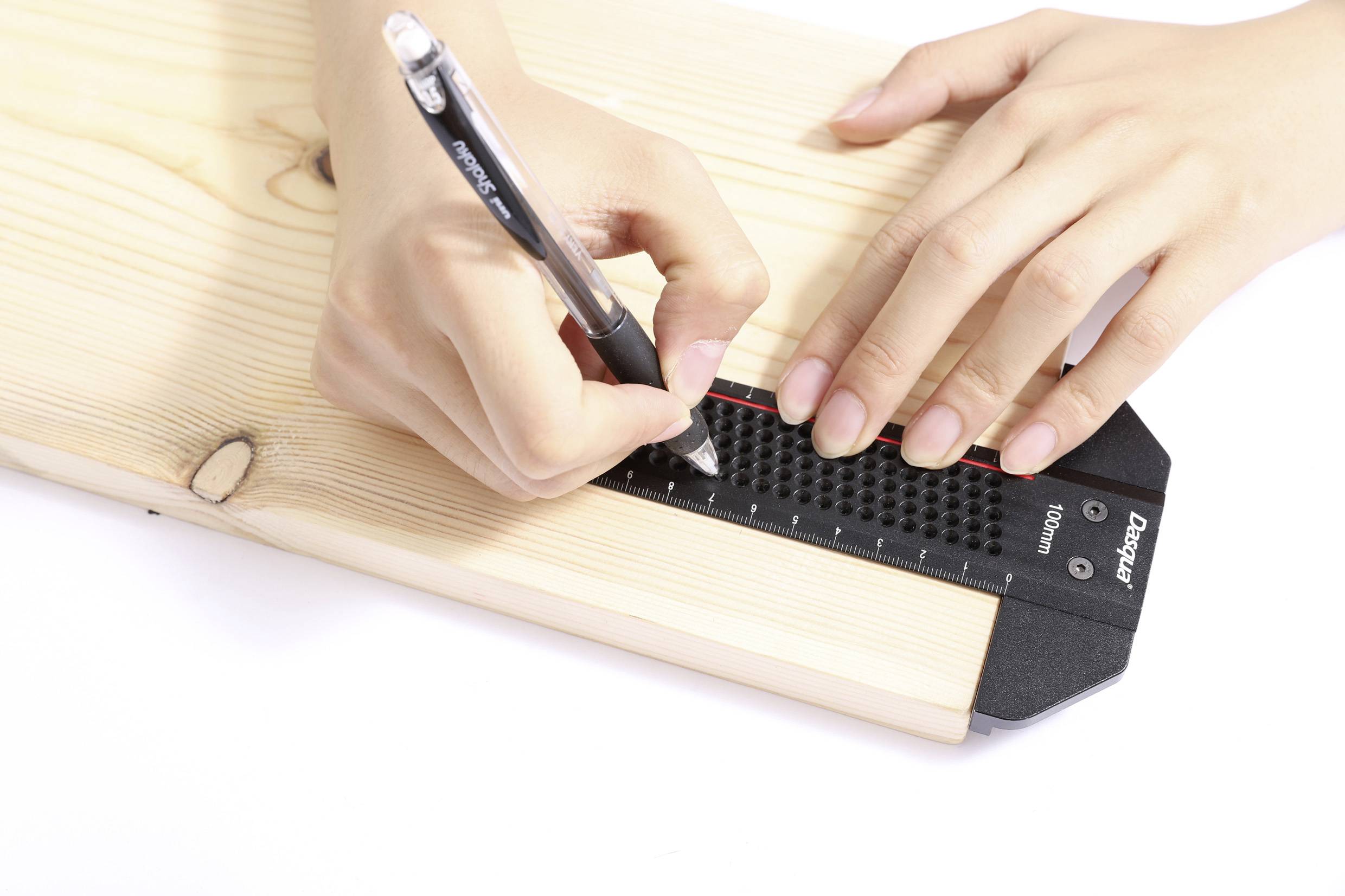 Deux mains mesurent et marquent une planche en bois à l'aide d'une règle noire et d'un stylo, indiquant une activité liée au travail du bois ou à la construction.