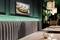 Intérieur de restaurant moderne avec des sièges rembourrés gris, une télévision murale présentant un plat, un éclairage chaleureux et des tables élégantes.