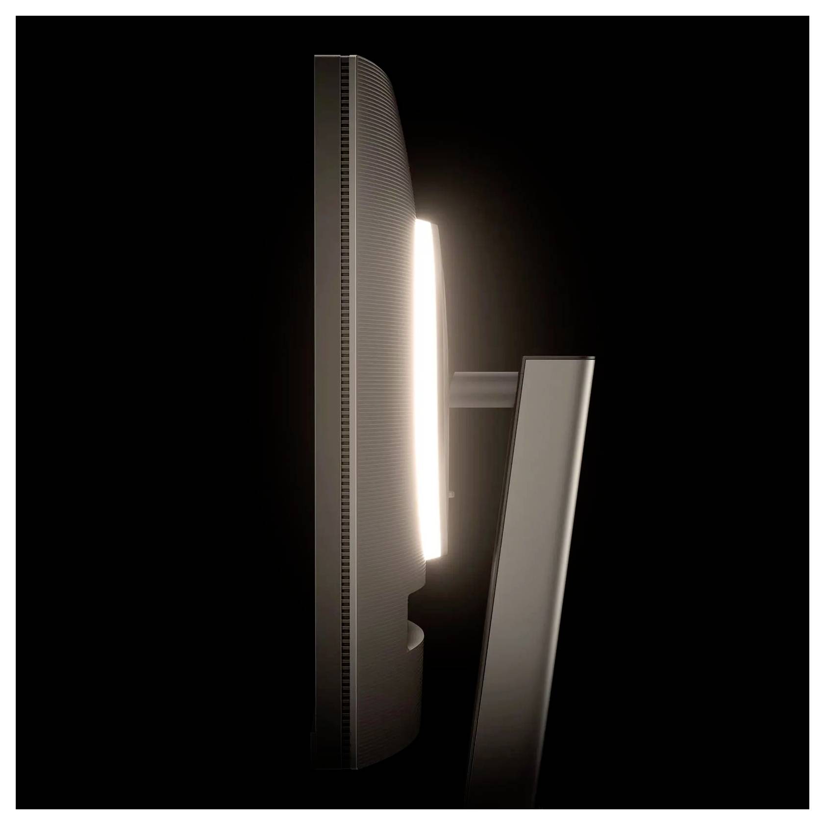 Un écran d'ordinateur élégant et fin, vu de profil, posé sur un support, avec un rétroéclairage subtil sur un fond sombre.