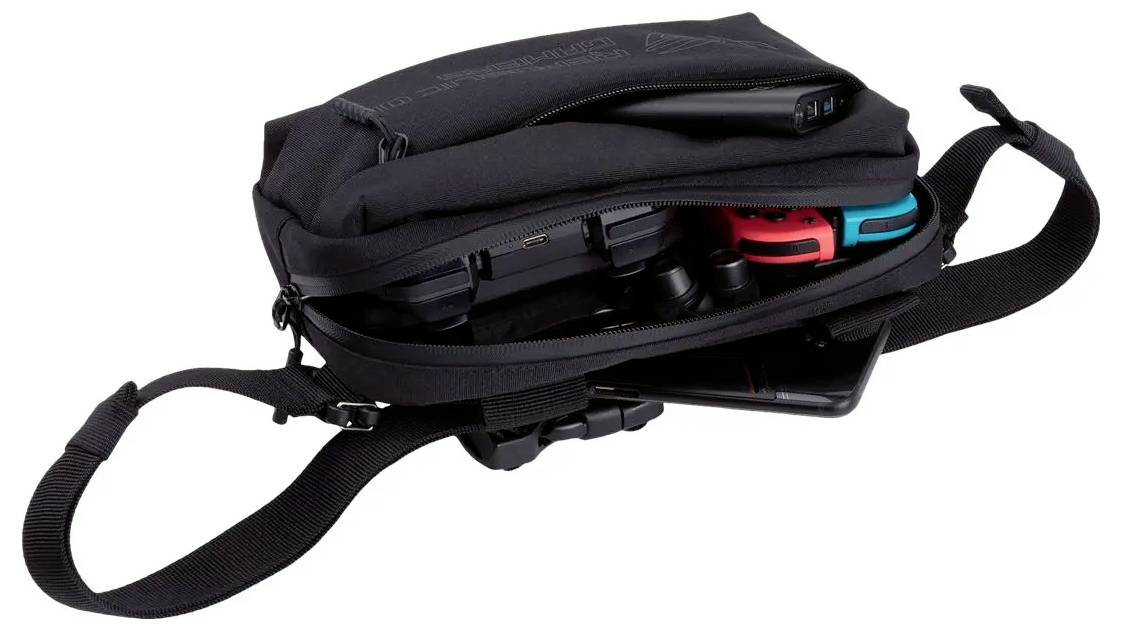 Un sac de voyage noir légèrement ouvert, laissant apparaître une console de jeux, deux manettes et un smartphone à l'intérieur.