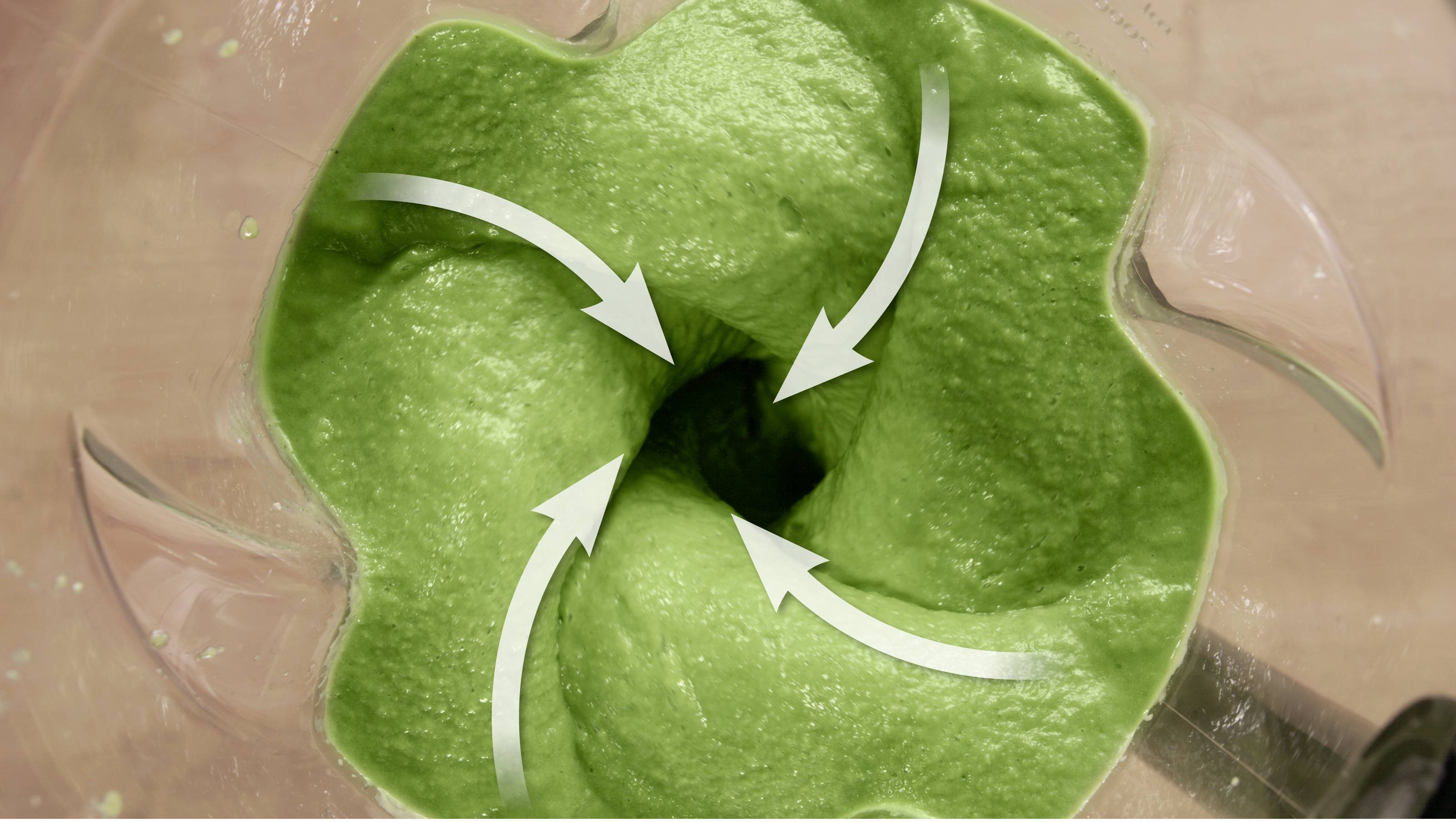 Vue de dessus des ingrédients d'un smoothie vert en train de se mélanger dans un blender. Trois flèches blanches indiquent le mouvement tourbillonnant à l'intérieur.