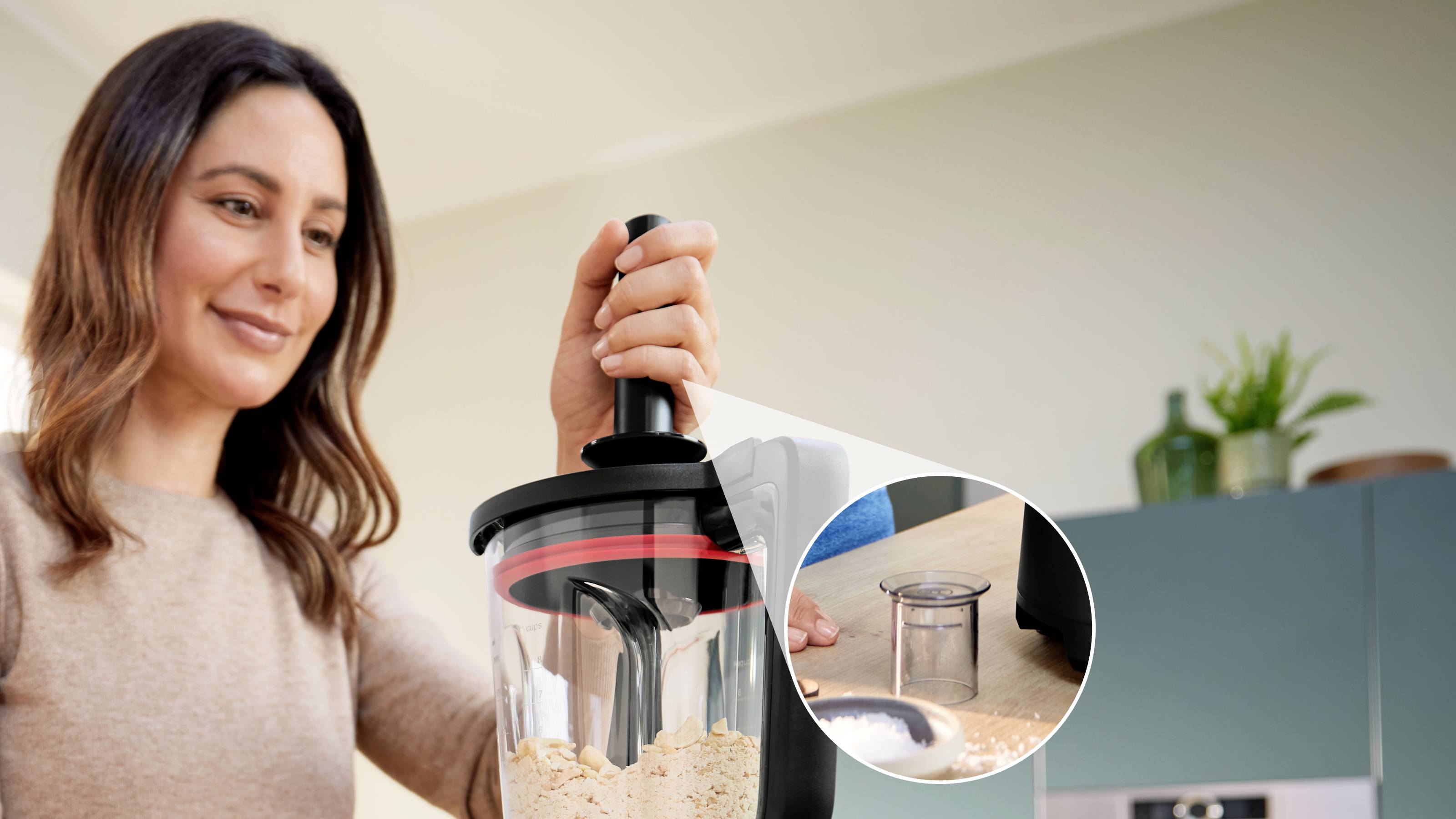 Une personne fait passer des aliments dans un robot culinaire noir et transparent. Un gros plan montre un petit récipient rond à côté de lui.