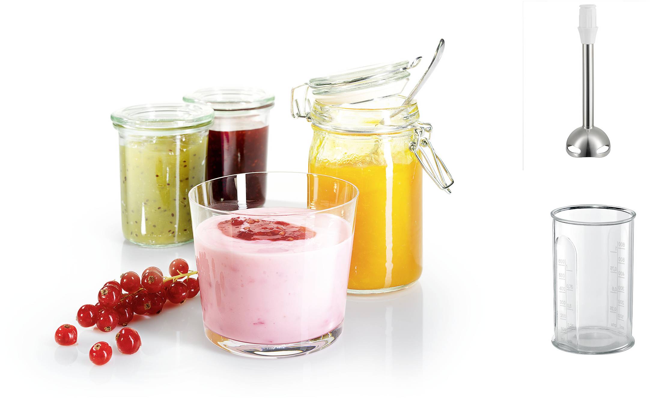 Smoothie rose dans un verre avec des baies rouges, à côté de bocaux de purées de fruits, mixeur plongeant et tasse à mesurer sur fond blanc.