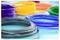 Des bobines colorées de filament pour impression 3D, comprenant du violet, du jaune, de l'orange, du bleu et du gris, sont disposées sur une surface bleu clair.