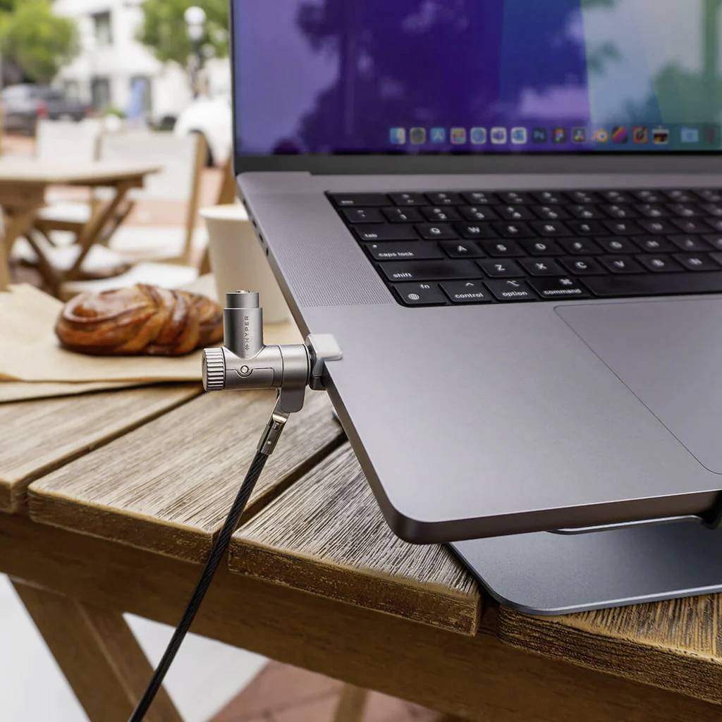 Un ordinateur portable posé sur une table de café avec un microphone branché, un croissant à côté, et une vue sur rue floue en arrière-plan.