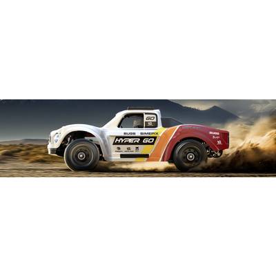 Un camion de course rouge et blanc portant l'inscription 'HYPER GO' roule à grande vitesse sur un terrain désertique, soulevant des nuages de poussière, avec des montagnes en arrière-plan.