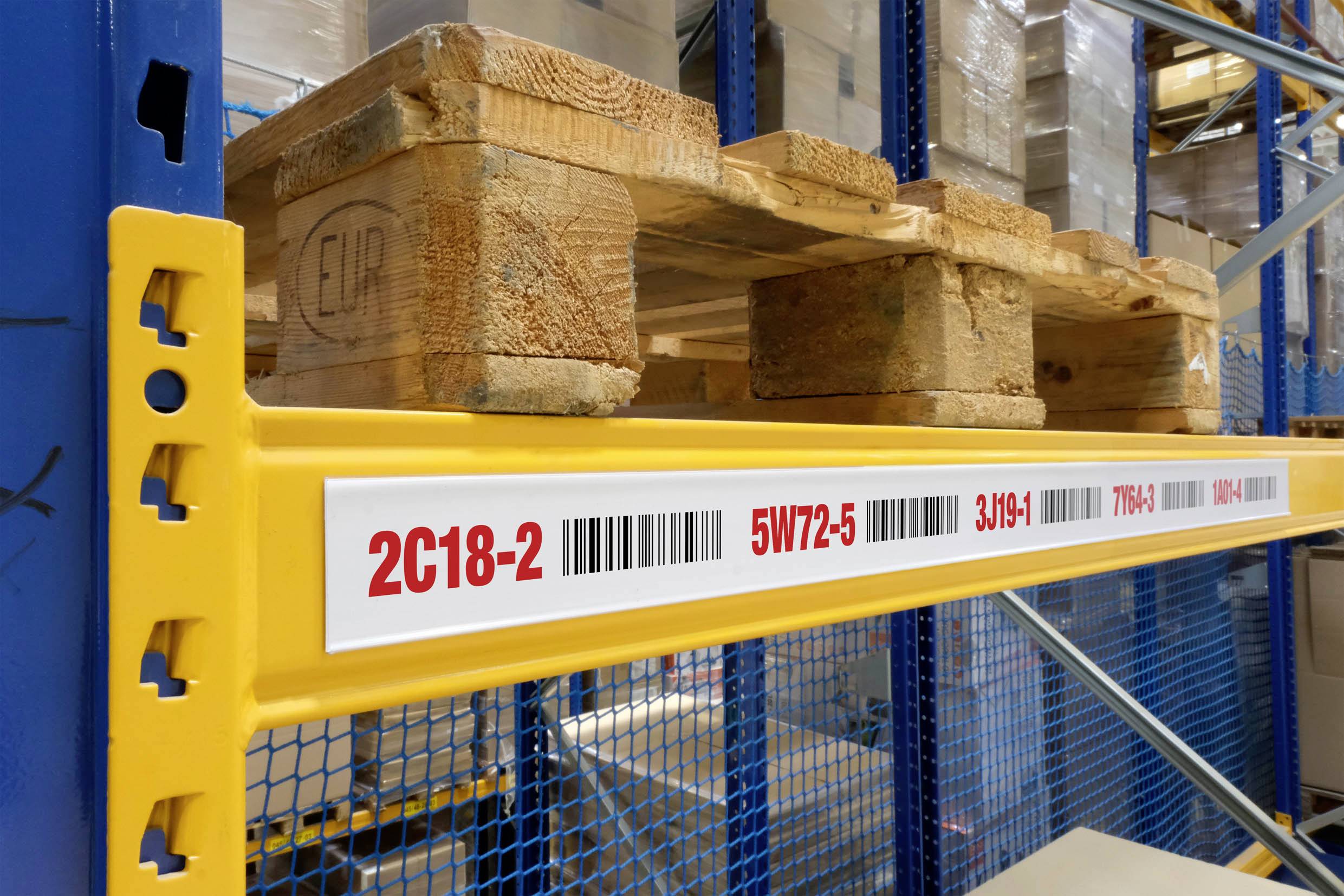 Étagère d'entrepôt avec une palette en bois rangée sur une poutre jaune. Une étiquette blanche affiche des codes-barres et des numéros : « 2C18-2 », « 5W72-5 », « 3JH9-4 ».