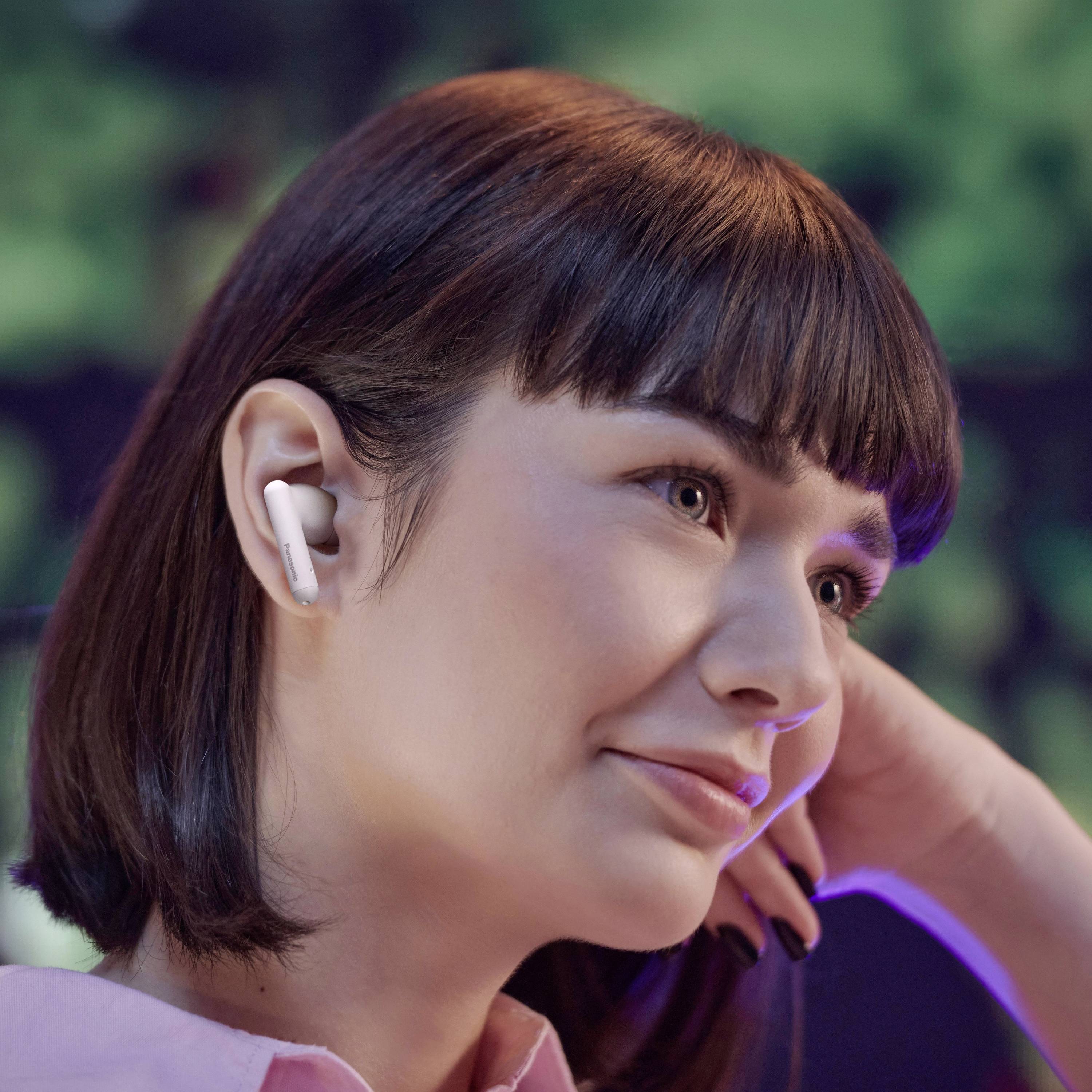 Une personne portant des écouteurs sans fil sourit, regardant vers l'avant. L'arrière-plan est flou, suggérant une ambiance détendue ou contemplative.