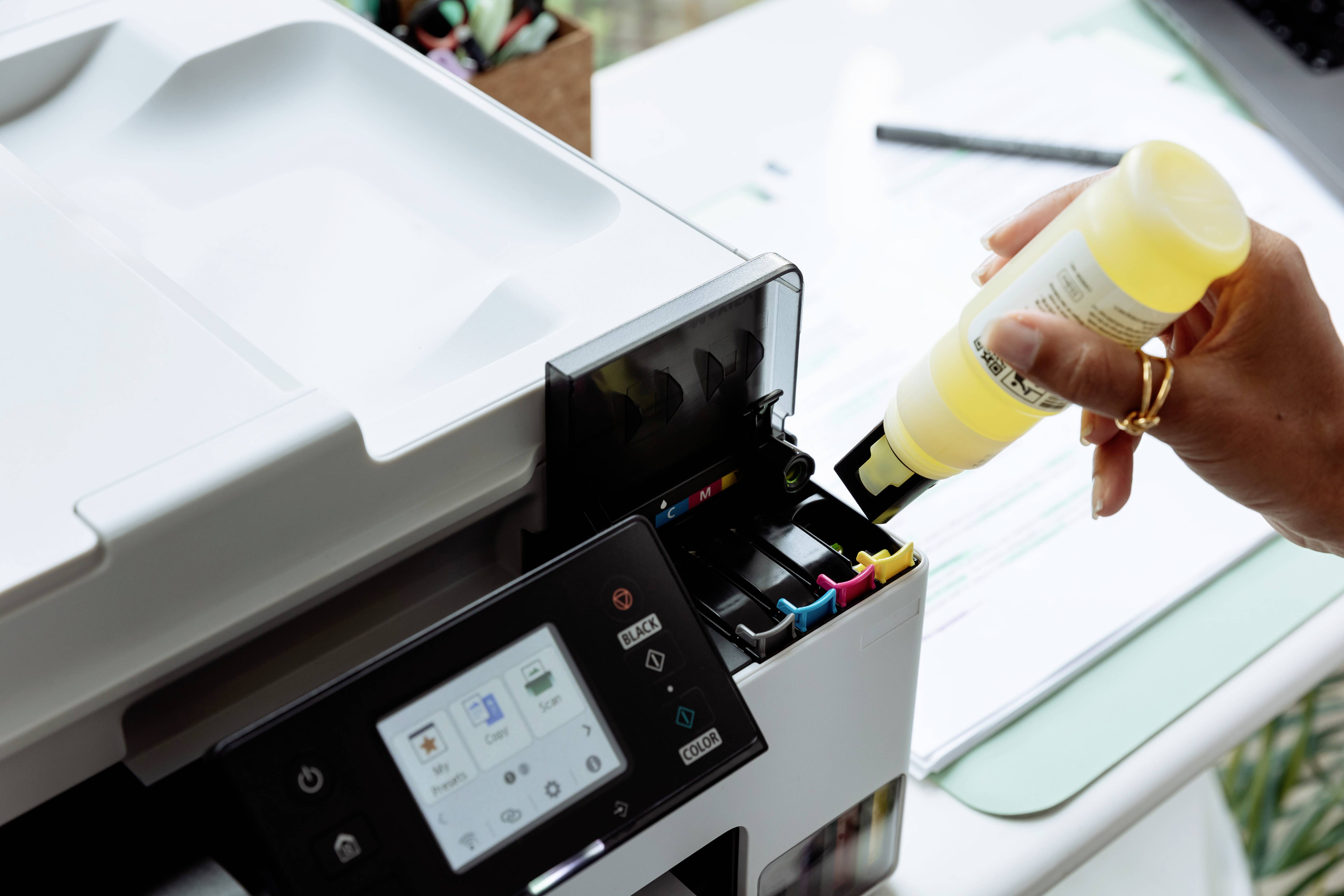 Une personne recharge une imprimante à jet d'encre avec de l'encre jaune, montrant l'écran de l'imprimante et la zone du compartiment de cartouche d'encre.