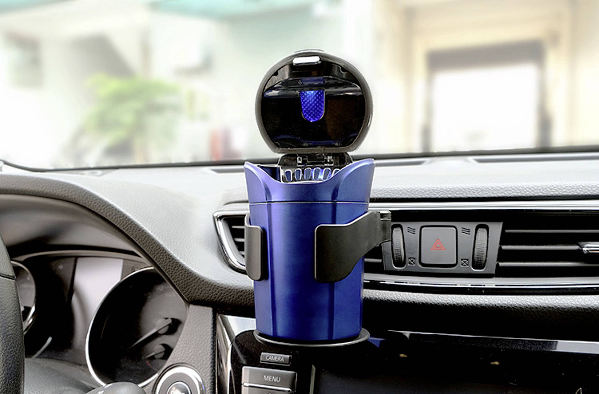 Un purificateur d'air bleu pour voiture monté sur le tableau de bord d'un véhicule, avec son couvercle ouvert, montrant un petit filtre bleu à l'intérieur, près des commandes de la voiture.