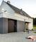 Une maison moderne avec un garage. Une main tient un appareil de mesure émettant une grille laser bleue en direction de la maison, illustrant la mesure de distance.
