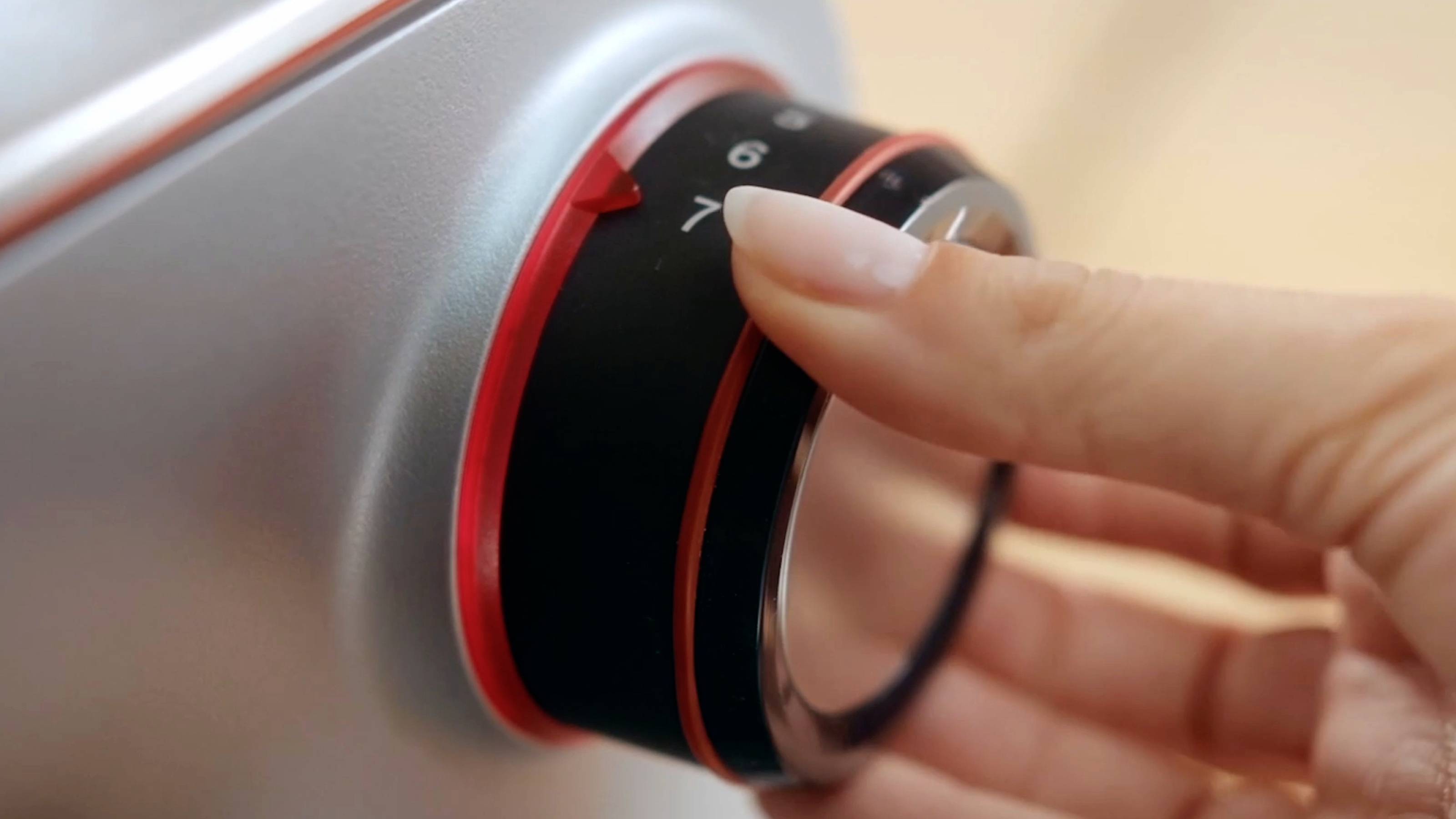 Une main tournant un cadran circulaire sur un appareil métallique, ajustant les réglages avec un souci de précision et de contrôle.