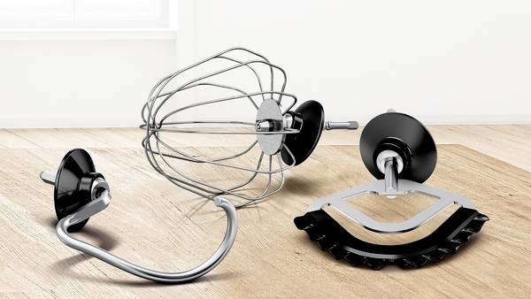 Trois accessoires de robot de cuisine, comprenant un fouet à fils, un crochet à pétrir et une palette plate, sont disposés sur une surface en bois.