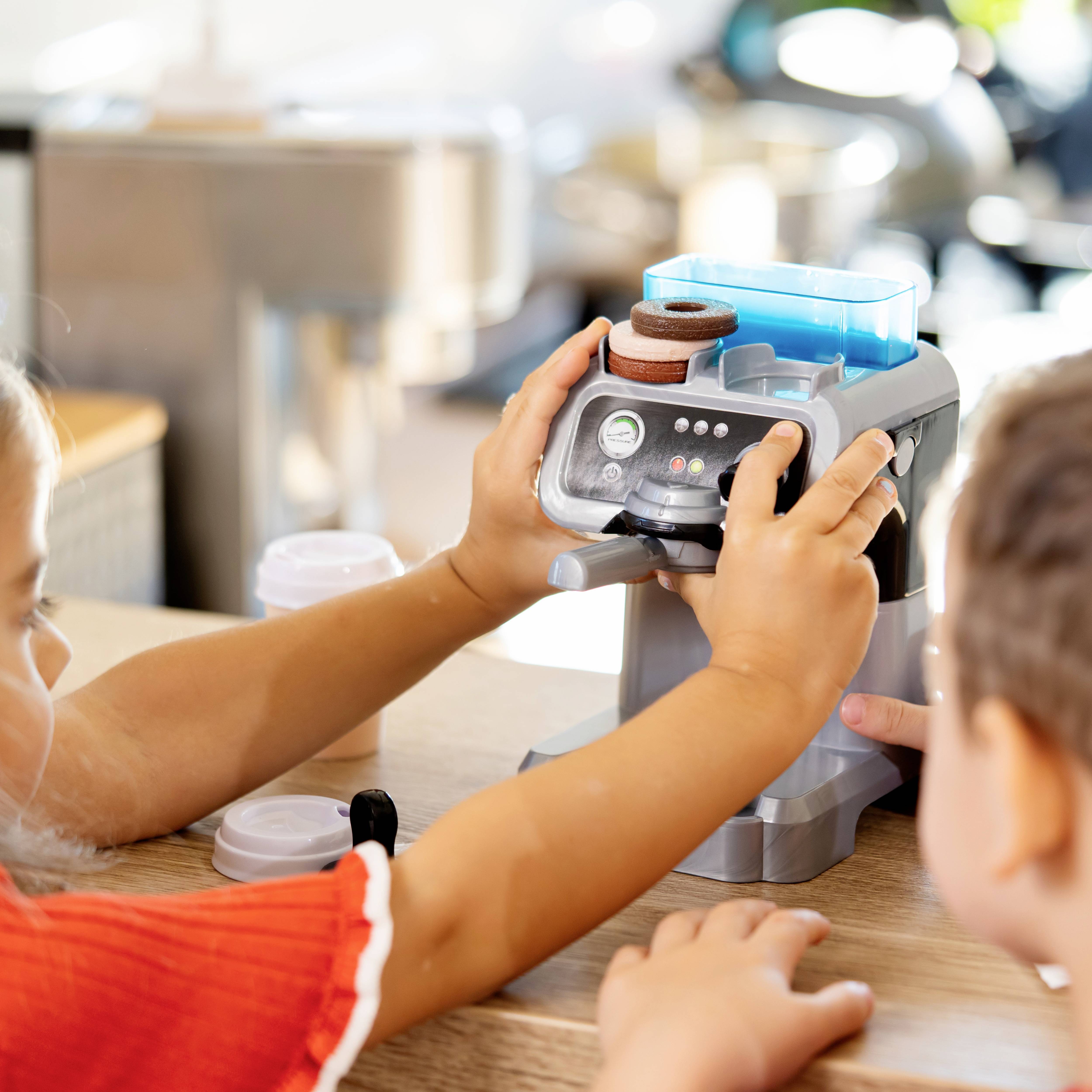 Des enfants jouent avec un distributeur de boissons factice sur une table, en appuyant sur des boutons pour créer des boissons imaginaires.