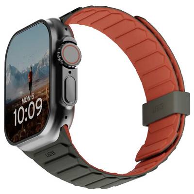 Montre connectée avec une sangle rouge et noire affichant un cadran numérique indiquant 'LUN 5' et '10:09'. Paysage de montagne en arrière-plan.