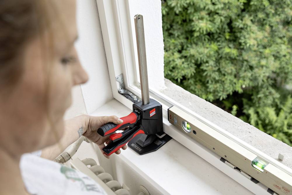 Une personne utilisant un serre-joint et un niveau sur un chambranle de fenêtre pour vérifier l'alignement, avec de la verdure visible à l'extérieur.