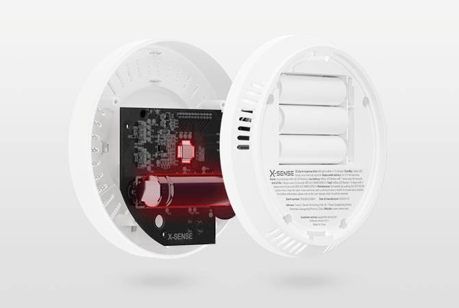 Un détecteur de fumée est représenté ouvert, montrant ses composants internes, notamment la carte de circuit imprimé, le compartiment de la batterie et les capteurs.