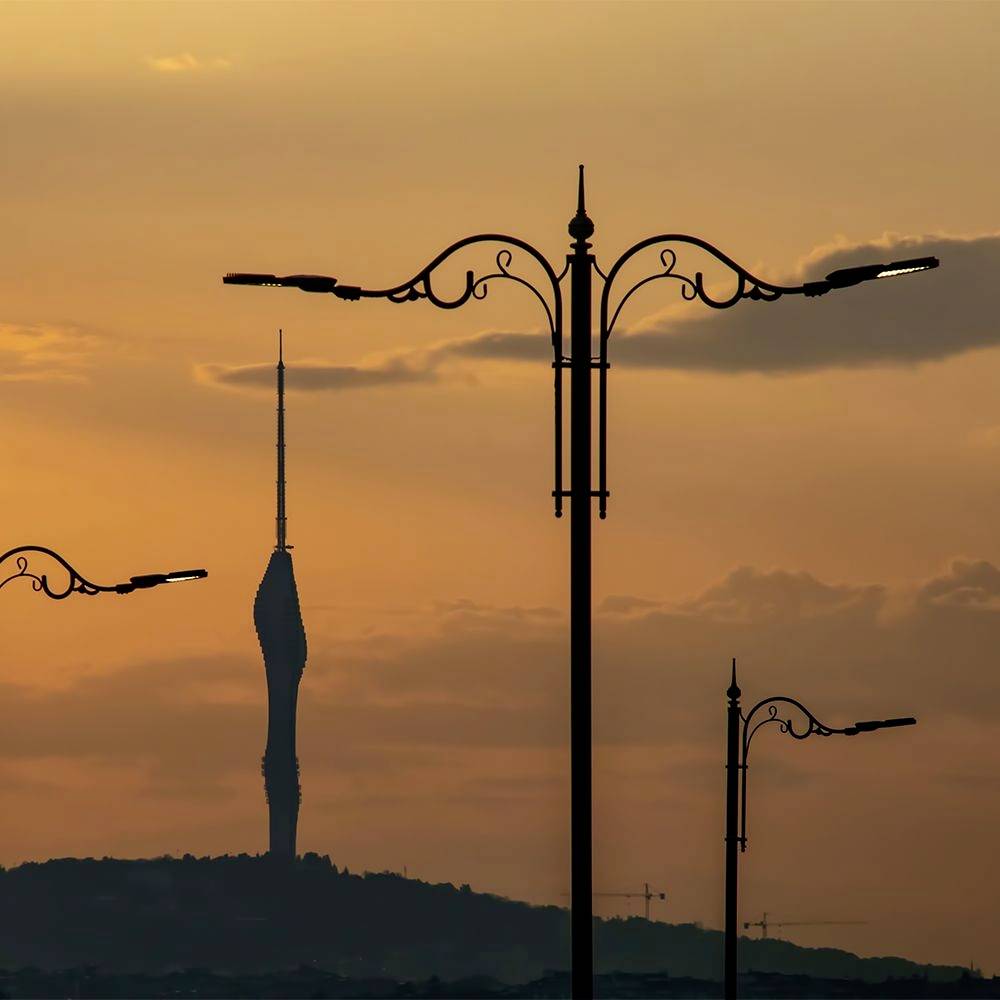 L'image montre une silhouette d'un horizon urbain au coucher du soleil, avec des lampadaires en évidence au premier plan et une tour haute à l'arrière-plan.