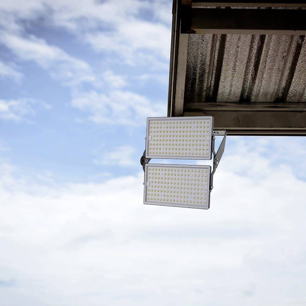 Projecteur LED extérieur fixé à une structure métallique contre un ciel bleu parsemé de nuages.