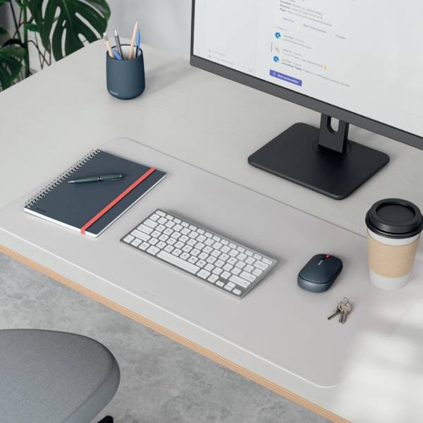 Un espace de travail minimaliste comprenant un écran d'ordinateur, un clavier, un carnet, des stylos, une tasse de café et une souris sur un bureau en bois clair.