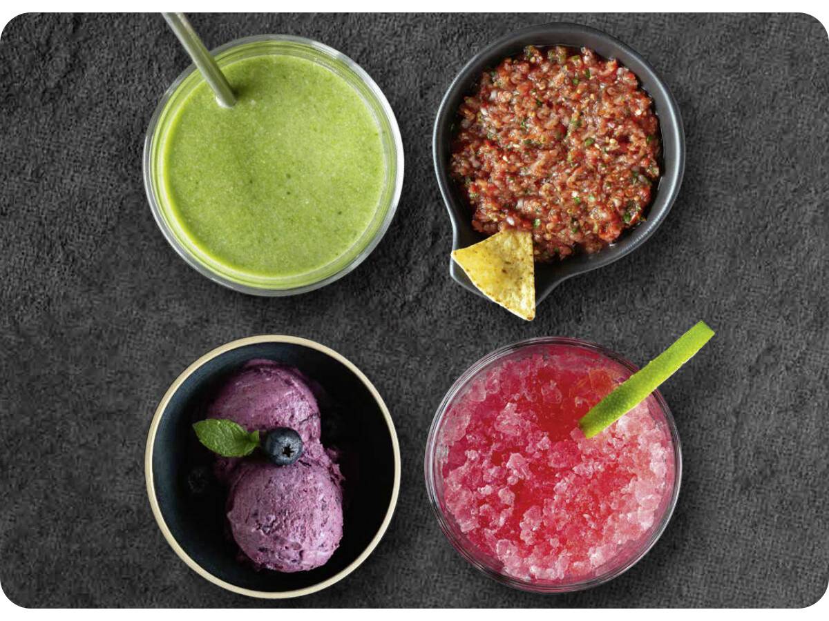 Quatre bols sur une surface sombre, contenant un smoothie vert, une salsa rouge avec une chips, une glace violette aux baies, et un slush rose avec un citron vert.