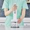 Une personne utilisant un mixeur plongeant pour écraser des glaçons dans un environnement de cuisine, portant une chemise vert clair.