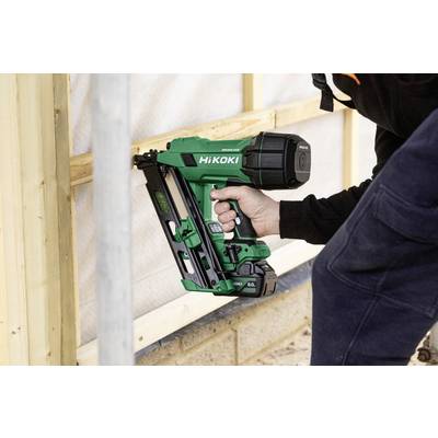 Une personne utilise un cloueur HiKOKI vert pour fixer des cadres en bois sur un chantier de construction extérieur.