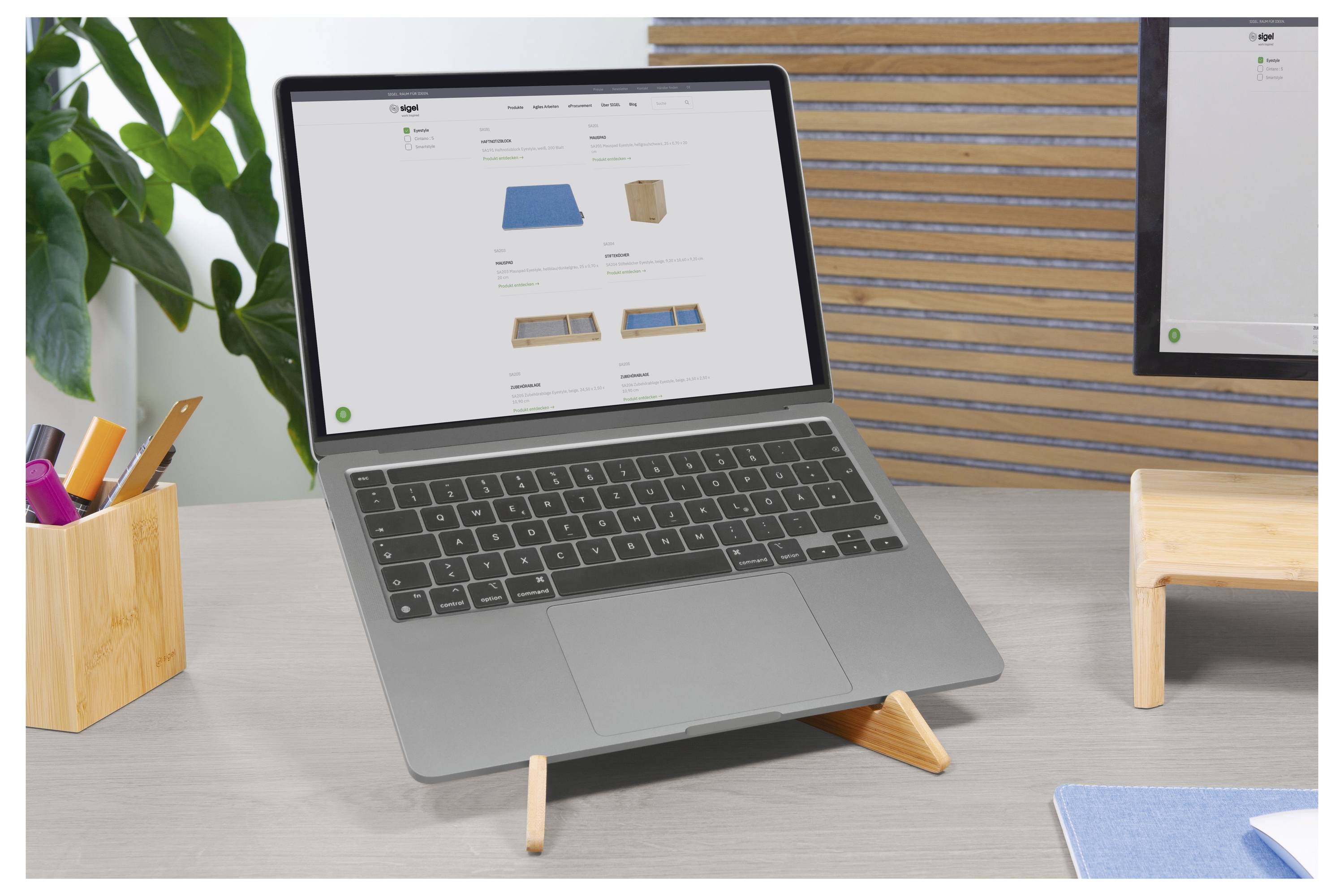 Ordinateur portable sur un bureau avec un catalogue de produits affiché à l'écran, entouré de fournitures de bureau et d'une plante dans un espace de travail propre.