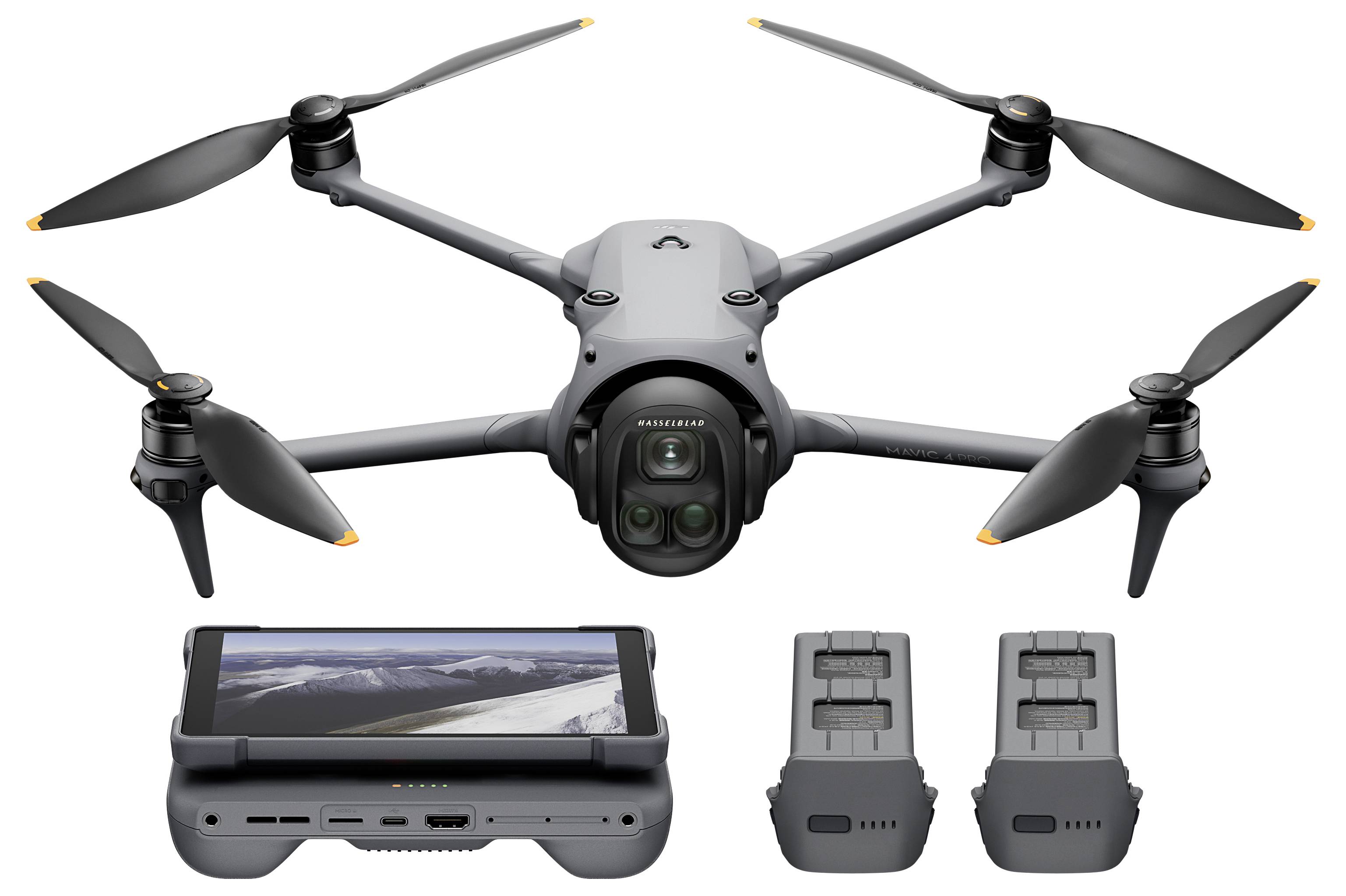 Un drone à quatre hélices, avec une caméra avant ; en dessous, deux batteries et une console avec un écran affichant un paysage montagneux.