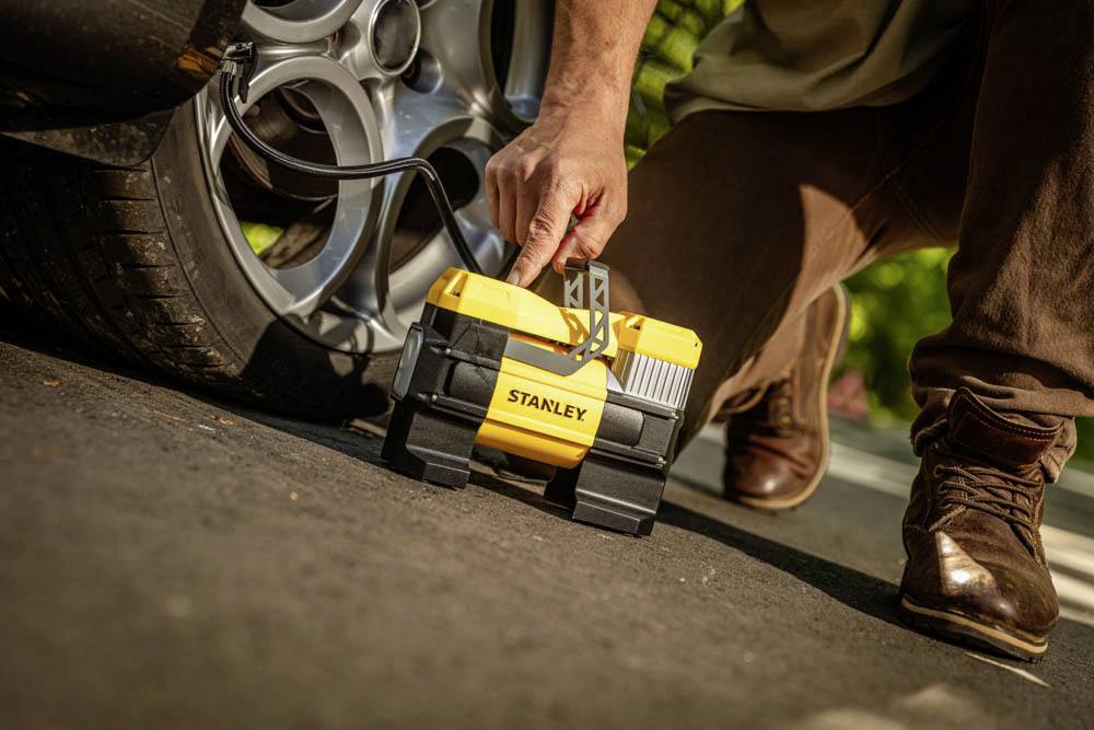 Une personne utilise un compresseur d'air portable jaune pour gonfler un pneu de voiture sur une route ensoleillée.