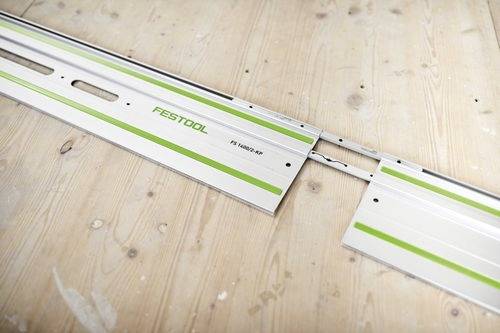Rail de guidage Festool en métal avec des rayures vertes sur un sol en bois, présentant des sections imbriquées pour une extension sans couture.