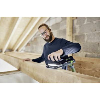 Une personne portant des lunettes de sécurité et des écouteurs utilise un outil de ponçage sur une poutre en bois dans une zone de construction.