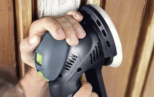 Une personne utilisant une ponceuse électrique portative pour lisser des surfaces en bois.