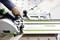 Une personne utilise une scie Festool avec un rail de guidage sur une surface en bois, réalisant des coupes précises. Un outil carré est également visible sur la table.