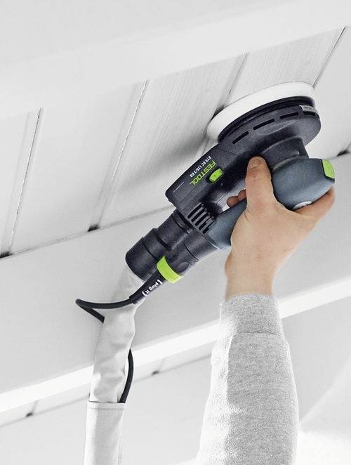 Une personne utilise un ponçeuse électrique pour lisser la surface d'un plafond en bois blanc, mettant en évidence une activité d'amélioration de l'habitat.