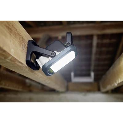 Une lampe de travail portable à LED fixée par une pince sur une poutre en bois, illuminant un espace de grenier avec des poutres apparentes et des tuiles de toit au-dessus.