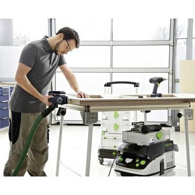 Une personne portant des lunettes de sécurité ponce une planche avec un outil électrique dans un atelier. Un extracteur de poussière est connecté, garantissant un espace de travail propre.
