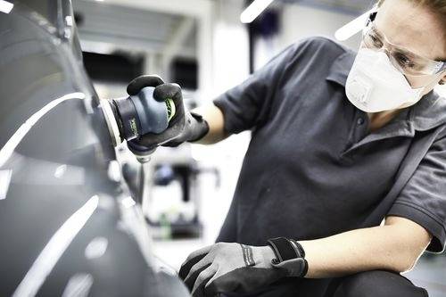 Une personne portant un équipement de protection polit la surface d'une voiture dans un atelier, illustrant un environnement de maintenance ou de réparation automobile.