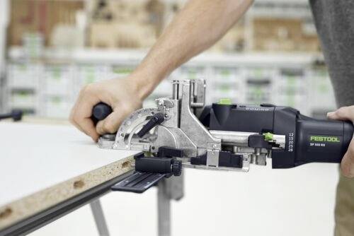 Une personne utilise un outil électrique Festool pour couper un morceau de bois, démontrant une mesure précise et un contrôle dans un environnement d'atelier.