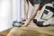 Une personne utilise un outil électrique pour couper le bas d'une porte tout en étant accroupie sur un plancher en bois, concentrée sur des travaux de rénovation ou d'amélioration domiciliaire.
