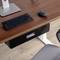 Un bureau en bois avec un clavier et une souris noirs. Un support argenté est placé à gauche. Une chaise de bureau grise est partiellement visible en bas.