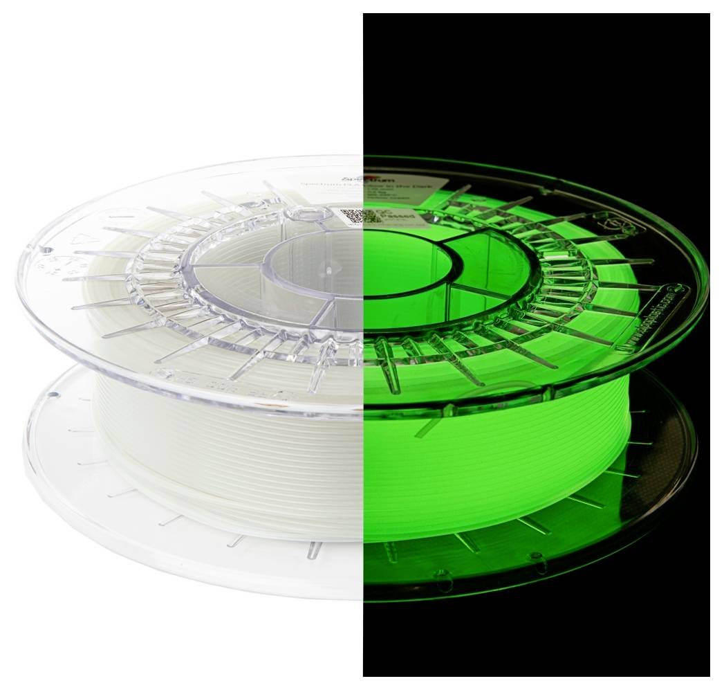 La moitié d'une bobine de filament d'imprimante 3D est représentée en train de briller en vert dans l'obscurité, tandis que l'autre moitié apparaît blanche à la lumière.