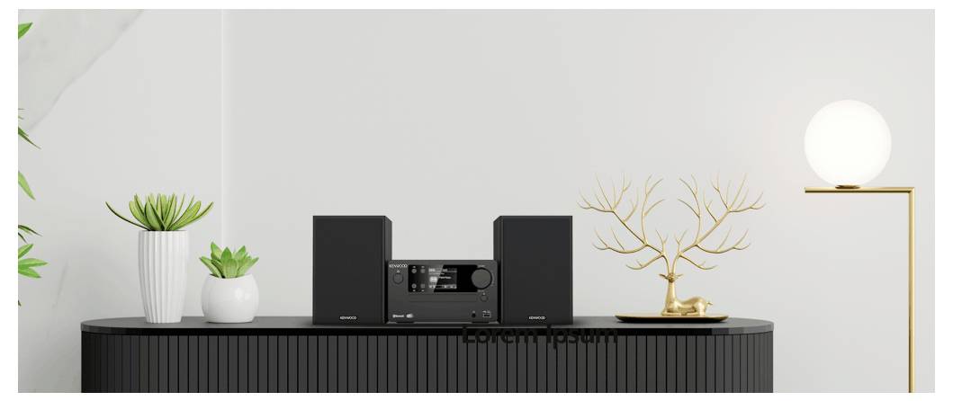 Un système stéréo moderne est posé sur une console noir élégante, encadré par des plantes en pot et une sculpture décorative dorée sous une lumière tamisée.