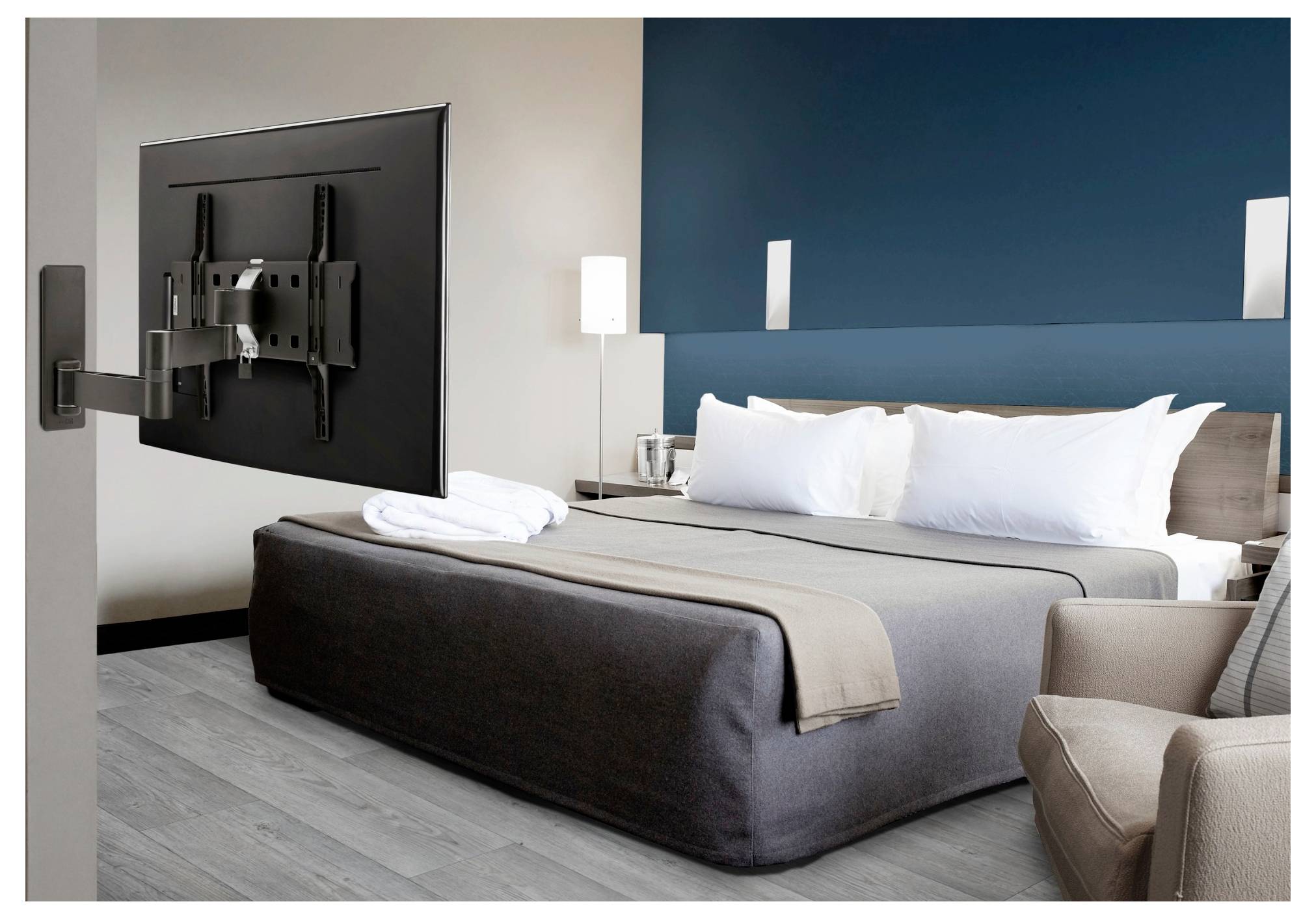 Une chambre d'hôtel moderne avec un lit king-size, de la literie blanche et grise, un mur d'accent bleu-vert, une télévision murale, un fauteuil et des lampes de chevet.